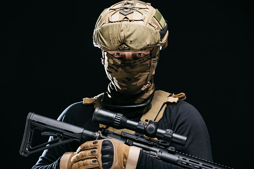 Photo of a confident and courageous military man on a dark isolated background in a camouflage uniform and with a weapon. The concept of a strong and invincible army.