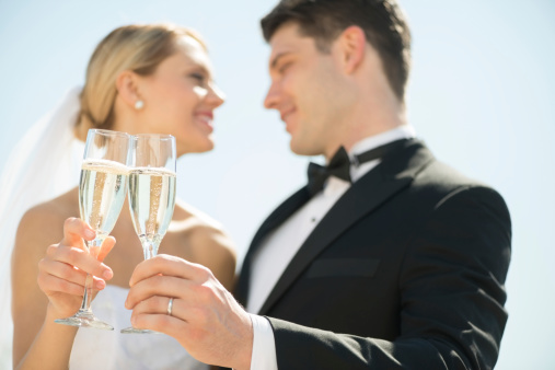 Low angle view of young bride and groom toasting champagne flutes against sky