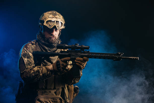istock A courageous soldier in a protective combat uniform with a machine gun standing on a dark background, shrouded in smoke. War and military concept. 1764730329