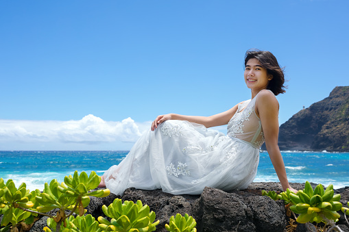 Teen girl in white dress sitting on lava rocks along Hawaiian coast at Makapu'u beach