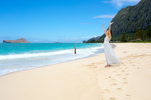 Teen girl in white dress on Hawaiian beack, arms raisedin worship or feeling the ocean breeze