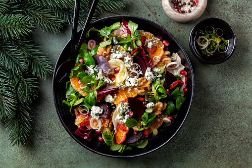 Top view of winter Christmas salad with beetroot, oranges, walnuts, pomegranate, dried cranberries, lettuce, blue cheese. Spices. Honey and olive oil dressing.