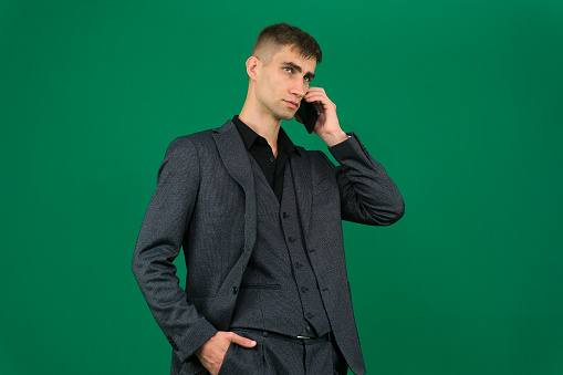 emotions of handsome man guy on a green background chromakey close-up dark hair young man. phone in hand talk dial SMS online call gadget boss work advertising