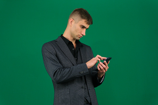 emotions of a handsome man guy on a green background chromakey close-up dark hair young man. phone in hand talk dial SMS online call gadget boss work ad