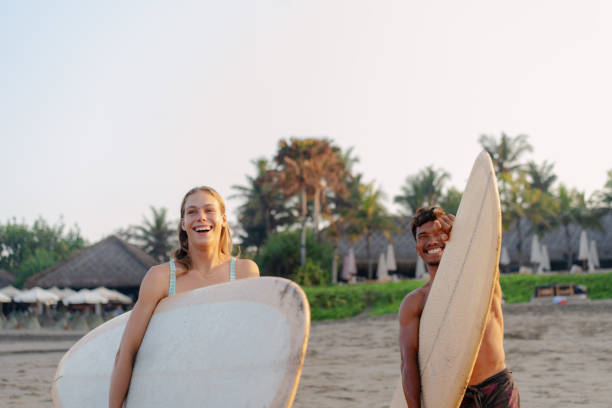 white female and male carrying surfboard looking at the ocean to surf - bali male beautiful ethnicity imagens e fotografias de stock