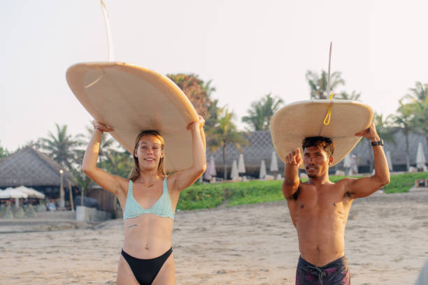 weiße frau und mann tragen surfbrett und schauen auf den ozean zum surfen - bali male beautiful ethnicity stock-fotos und bilder