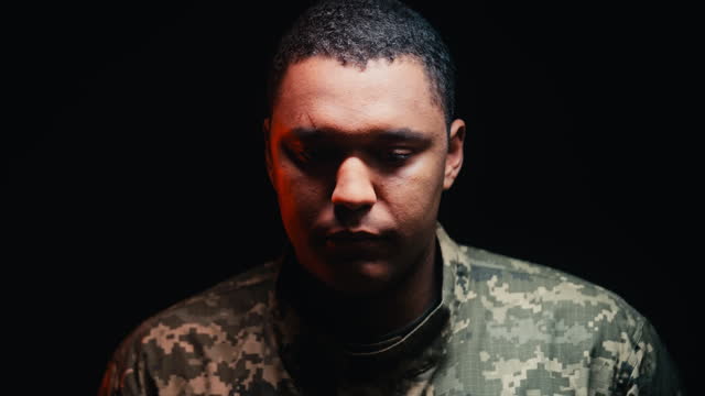 Serious African American serviceman standing in darkness, looking at camera