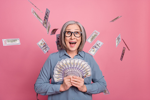 Photo of overjoyed pensioner lady wear trendy clothes hold bank cash savings salary jackpot isolated on pink color background.