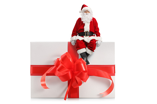 Full length portrait of a santa claus sitting on a big present box isolated on white background