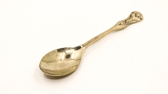 a shiny, clean and old antique bronze metal spoon used by royalty displayed for auction isolated in a white background