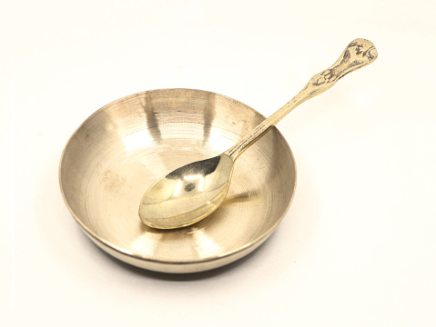 closeup of a shiny vintage bronze metal spoon and bowl used in luxury restaurant isolated on white background
