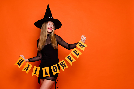 Photo of attractive blonde teen woman look empty space hold garland dressed black halloween clothes isolated on orange color background.