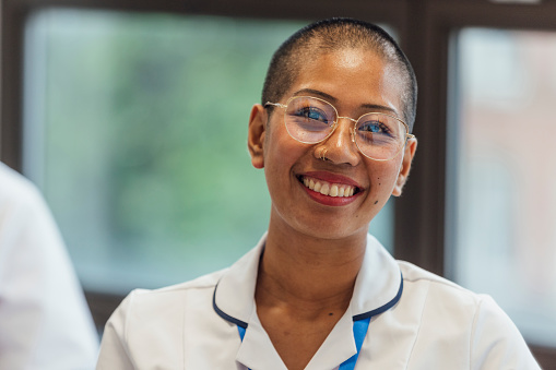 A portrait of a young female student nurse, standing in a hospital in Newcastle upon Tyne, North East England. She is looking at the camera and smiling.