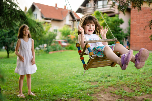 Two happy girls playing on a swing in the yard at summer day