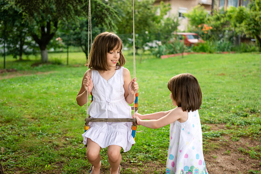 Happy sisters playing on a swing in the yard at summer day