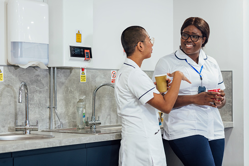Two student nurses wearing uniforms taking a break while working at a hospital They are standing on a break room holding hot drinks in Newcastle Upon Tyne, North East England.