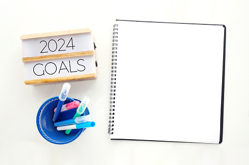 2024 goals on wood box and blank notebook paper on white marble background, business new year aim to success