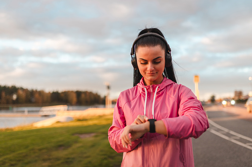 Young woman using her smartwatch while running outdoors. She is also wearing headphones.