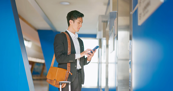 Close up asian male businessman scrolling mobile phone waiting for elevator while on business trip in the ariport