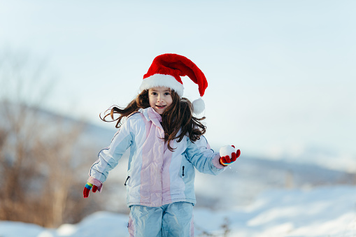 Little girl playing with snow in nature making a hearth shape snowball with her hands