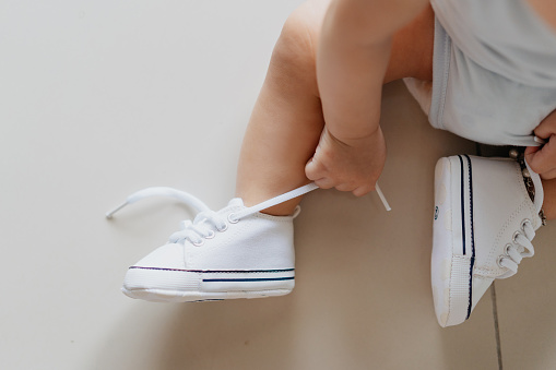 Close up shot of baby boy's feet with a pair of white shoes and sitting on the floor