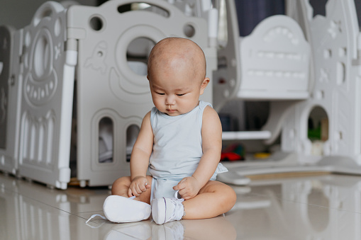 An Asian Chinese baby boy with a pair of white shoes and sitting on the floor