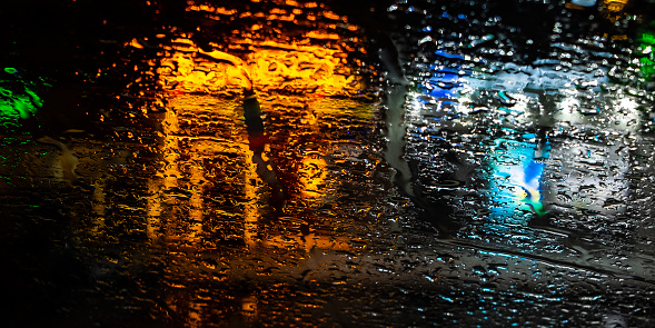 Blurred lights of the night city through drops on the glass. Selective focus on water drops on glass. Abstract background.