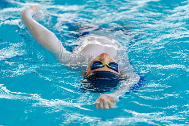 Young boy's dedication and enthusiasm as he practices backstroke swimming in a pool, preparing for a summer competition. Dressed in a swimsuit and equipped with swimming goggles. Focused concentration reflects the discipline and hard work training.