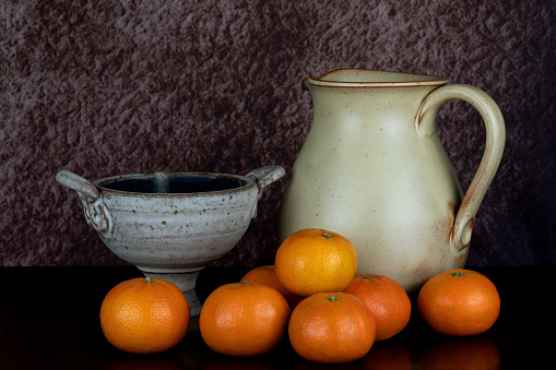 Pottery wine jug and chalice bowl with satsuma oranges on a polished wooden surface