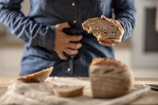 Woman can't eat bread and grain products because of gluten intolerance. A young celiac woman suffers from abdominal pain after eating fresh bread.