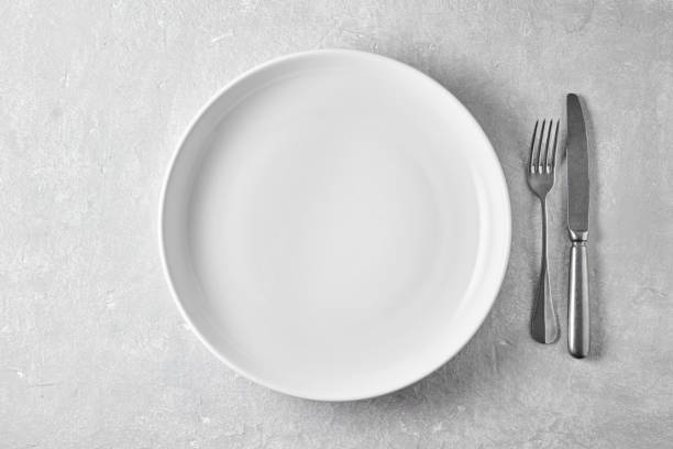 istock Empty white plate and fork with knife on a gray concrete table. Top view with copy space 1765048504