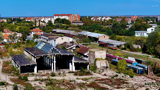 The overgrown and forsaken railway terrain, featuring aged train cars and crumbling infrastructure, stands as a silent testament to the passage of time amidst a thriving city setting.