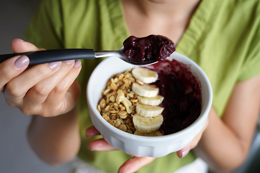 Young woman eating Brazilian acai from bowl with banana and granola as breakfast