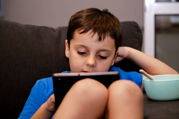 istock A boy sitting on a sofa at home playing with a tablet. Serious expression on his face. Concept of addiction to electronic games in young children. 1765118143