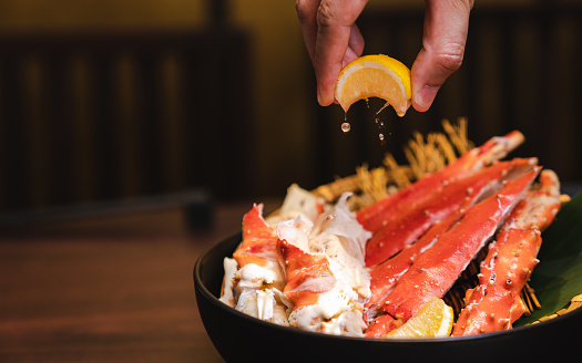 Steamed King crab in Japanese style in black bowl. Hand squeeze lemon with lemon juice drop.