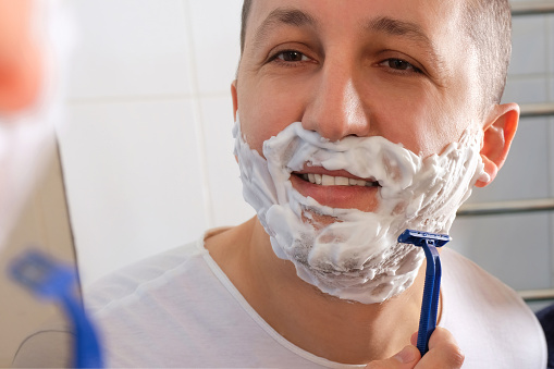 A young man shaves with a razor in front of a mirror. Skin care concept