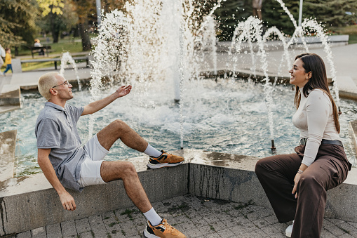 Two friends sitting by the water fountain and playing