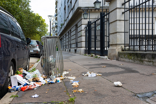 Paris, France: August 14'2023 : abandoned dirty garbage on a street in the city pollute the surrounding nature with garbage litter bin and residence building in background