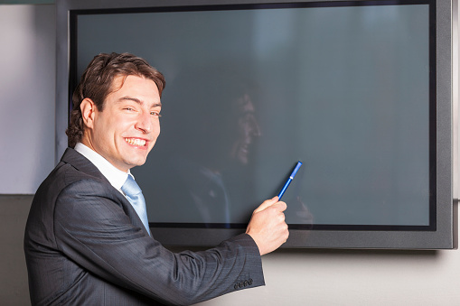 Portrait of happy businessman in front of blank plasma TV screen. Add your own design on screen. Model and Property released.