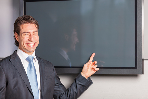 Portrait of happy businessman in front of blank plasma TV screen. Add your own design on screen. Model and Property released.