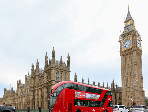 Famous London red double decker bus and traffic on Westminster Bridge about to pass Big Ben and the Houses of Parliament - London, UK