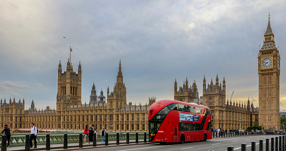 Panorama shot of famous red London bus crossing Westminster Bridge towards Big Ben and the Houses of Parliament - London, UK