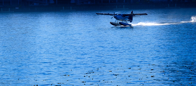 Sea airplane with pontoons taking off from water and flying propeller