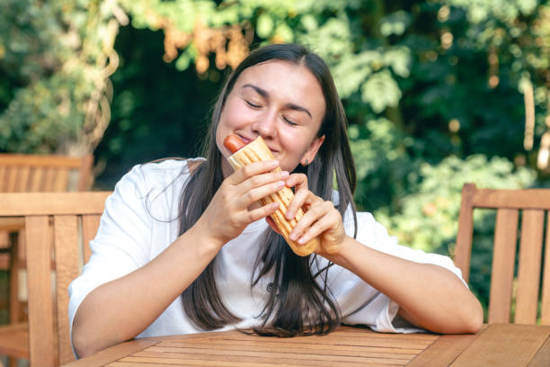 istock A young woman eats a hot dog on a cafe terrace. 1765226000
