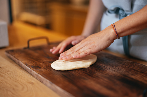Cropped photo of an unrecognizable woman working the dough on the wooden kitchen board, making small bread loaves.