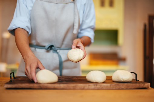 An anonymous female baker putting dough in a row on a wooden tray while standing at the kitchen desk.