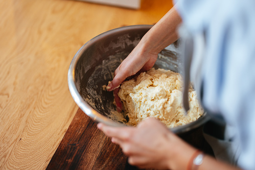 High angle view of an anonymous female baker making homemade bread while standing at wooden kitchen desk.