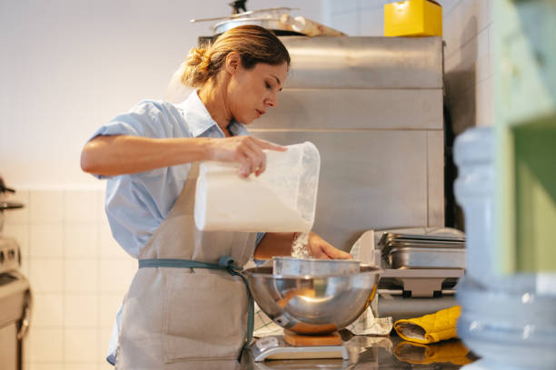 istock Beautiful Woman Adding Flour to the Bowl While Working in the Bakery 1765226596