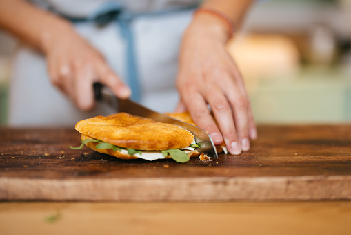 An anonymous female baker with apron making a tasty sandwich while standing at the kitchen desk.