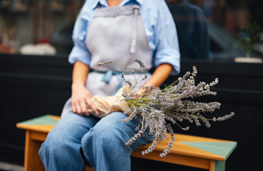 Unrecognizable woman in apron holding a bouquet of lavender while taking a break from working in the bakery shop.